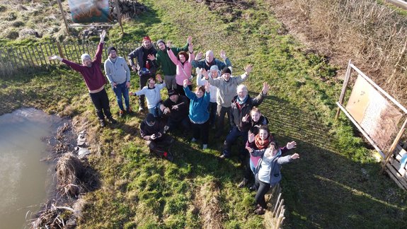 À côté de la mare et vus du ciel, des volontaires lèvent les bras en souriant