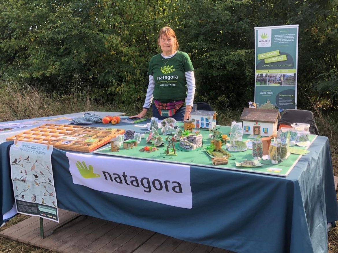 Une volontaire Natagora derrière un stand où sont présentés divers jeux éducatifs sur les oiseaux et la biodiversité au jardin