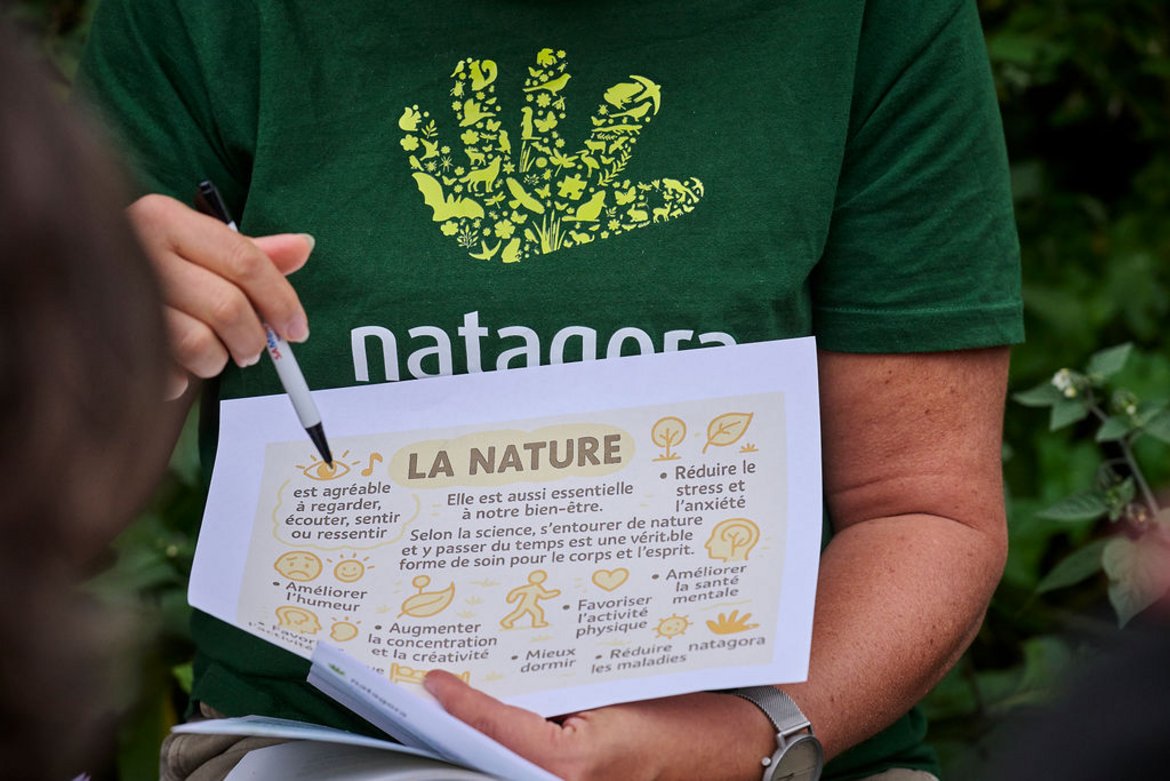 Gros plan sur une feuille tenue par une volontaire dont on voit le t-shirt floqué Natagora, feuille où sont décrit en facilitation graphique tous les bienfaits de la nature sur la santé