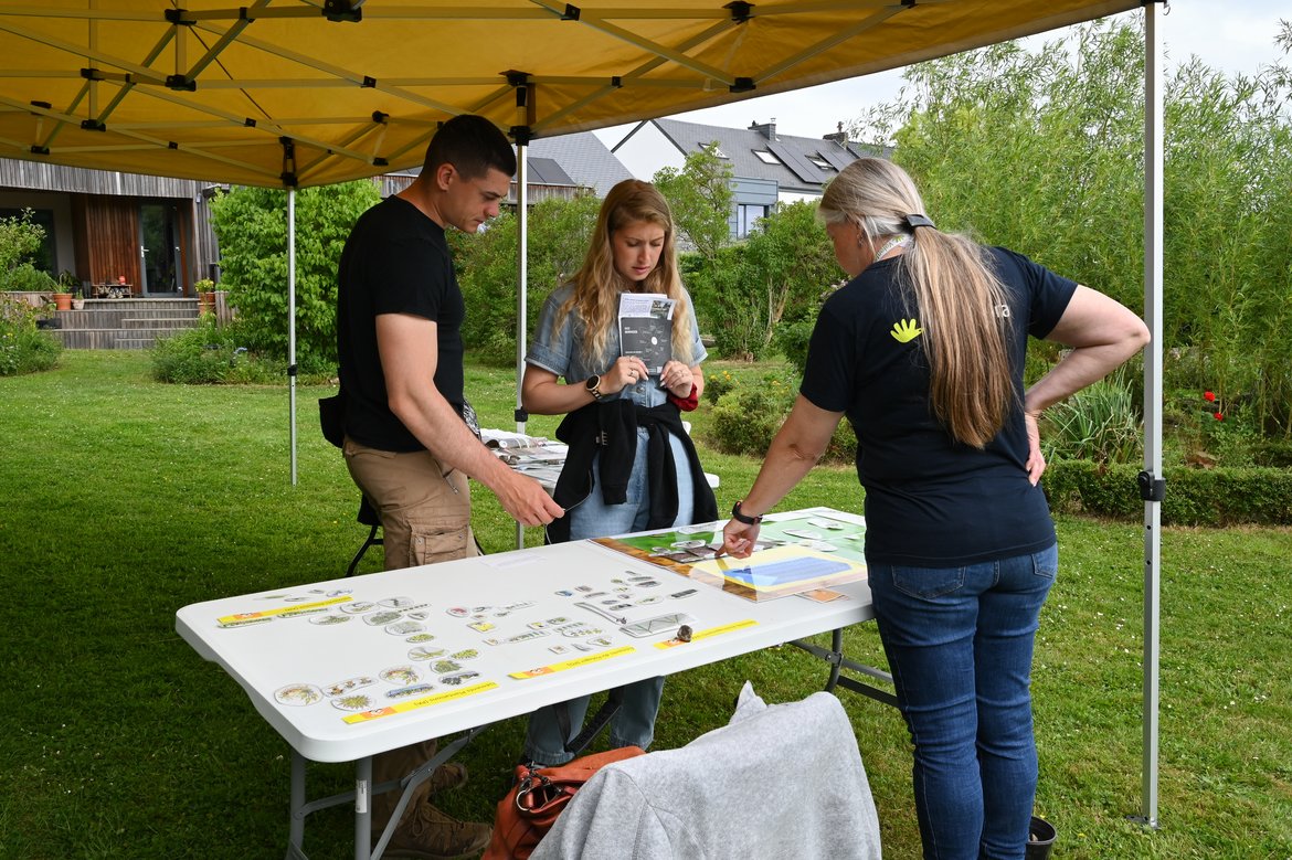 stand avec un jeu pour découvrir les aménagements favorisants la biodiversité dans un jardin. Une volontaire vue de dos aide un jeune couple vu de face qui en profite pour réfléchir à leur futur jardin